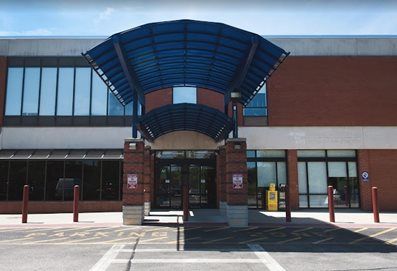 Brick building entrance with a blue awning, glass doors, and parking bollards.