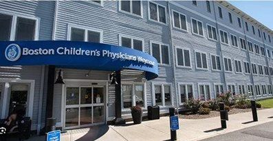 Boston Children's Physicians building entrance with a blue awning and glass doors. Gray exterior, windows.