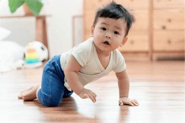 Baby crawling on a wooden floor, looking up with a surprised expression.