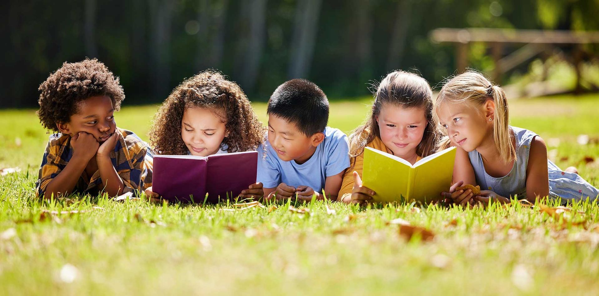 Kids reading books in the grass outside.