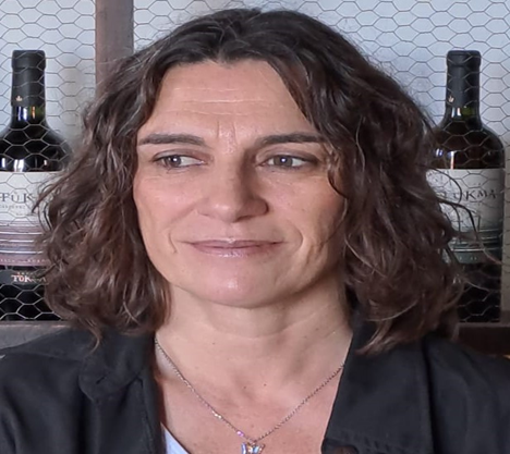 Mujer de pelo rizado frente a unas botellas de vino, mirando ligeramente hacia un lado.