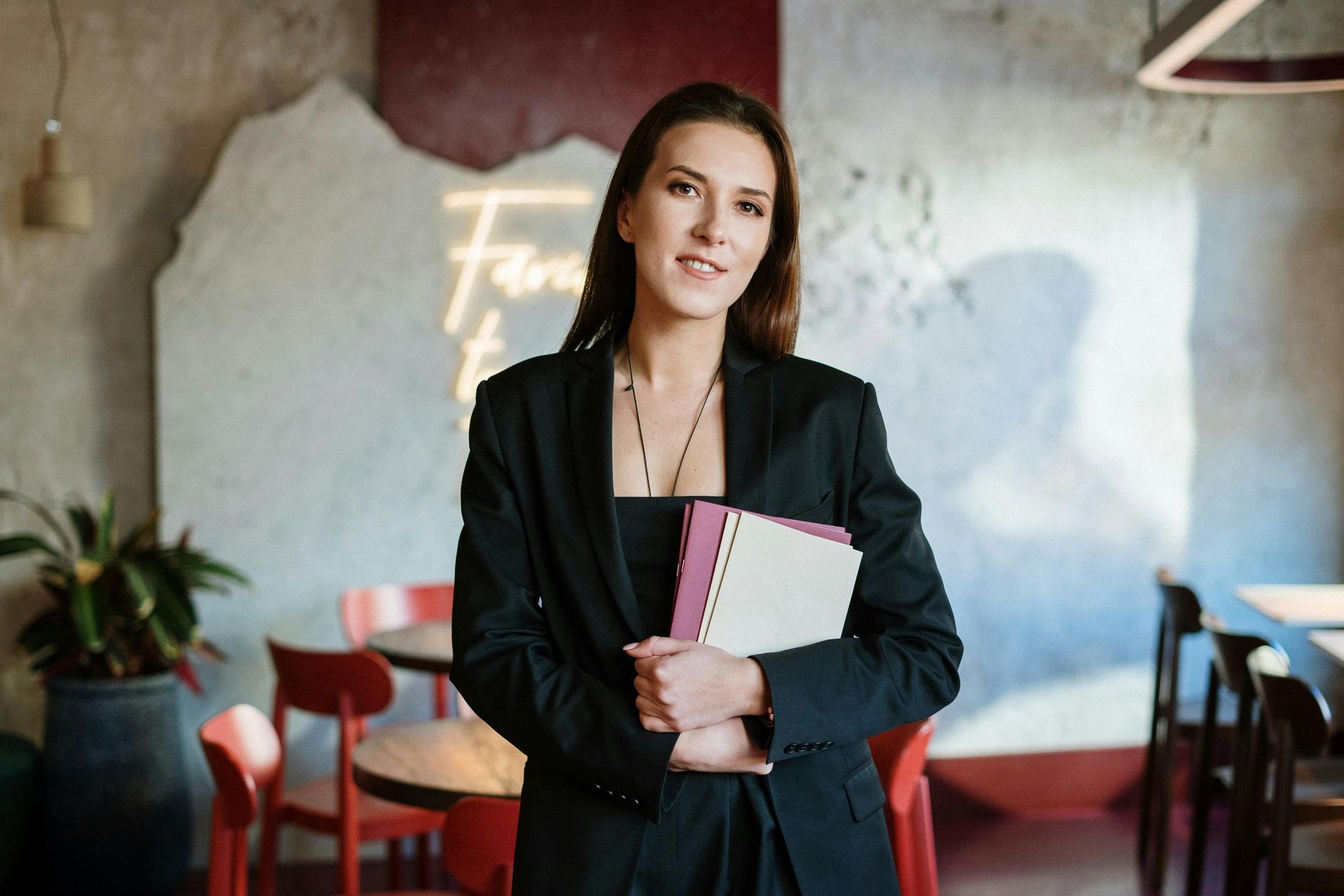 Una mujer con un traje negro sostiene un cuaderno en un restaurante.