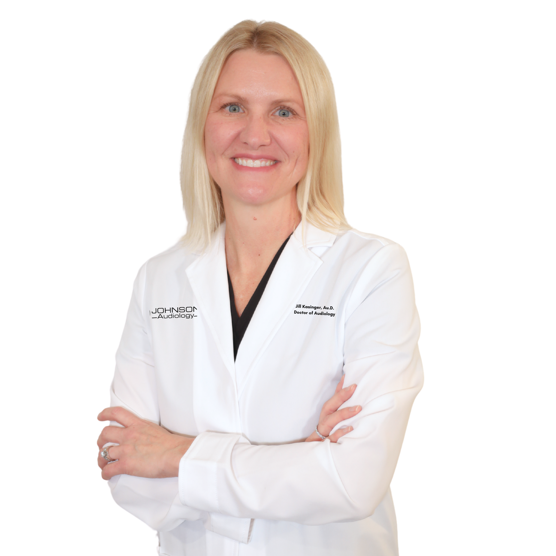 Smiling blonde woman in a white lab coat, arms crossed, medical setting.