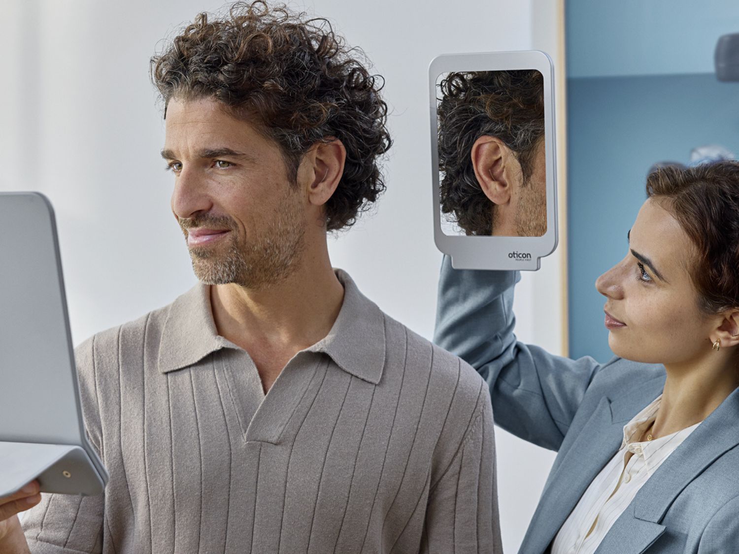 Person showing phone with urn image; another person looks on. Sunlight streams in.