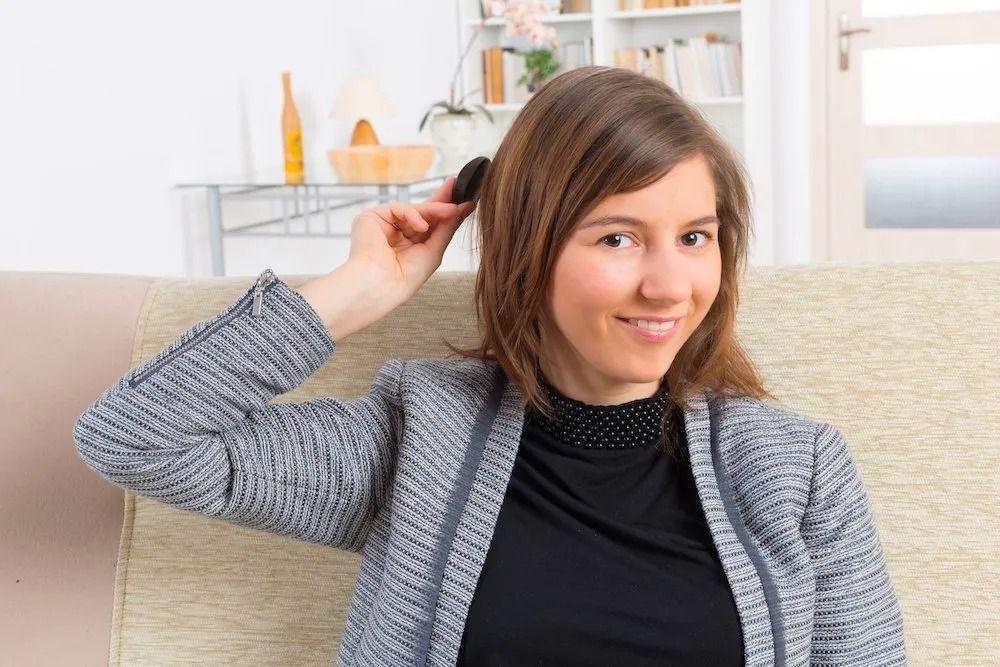 A woman is brushing her hair while sitting on a couch.