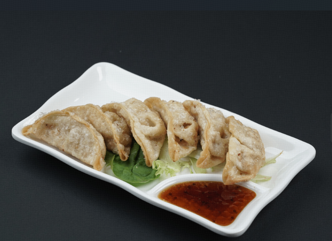 Fried dumplings on a white platter with green garnish and a red dipping sauce