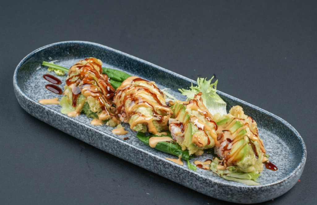 Grilled sushi rolls on a long oval plate, drizzled with sauce and garnished with greens