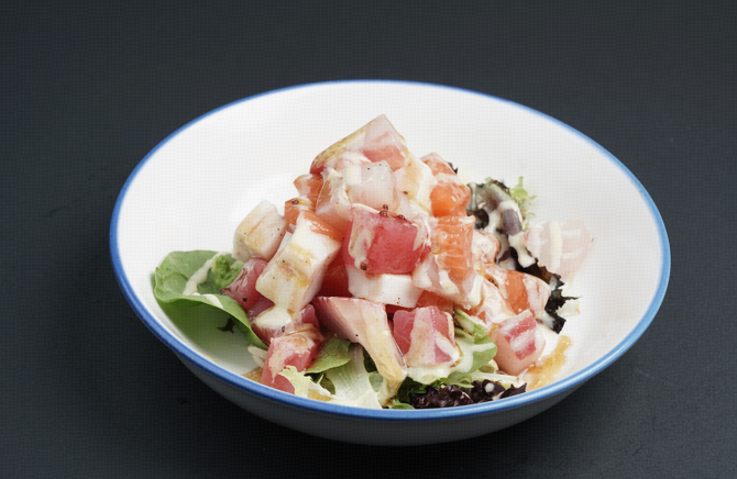 White bowl of salad with avocado, diced toppings, and creamy dressing on a dark table