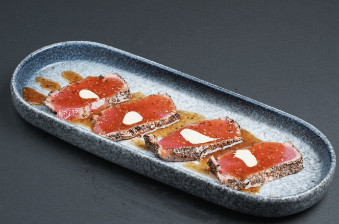Rectangular platter with red-glazed dessert slices topped with whipped cream and nuts