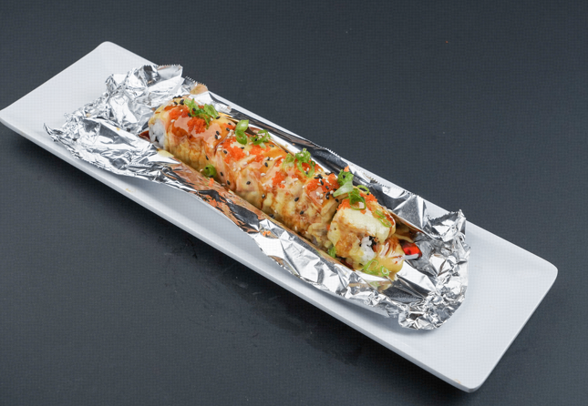 Grilled vegetable roll topped with herbs on foil-lined white plate