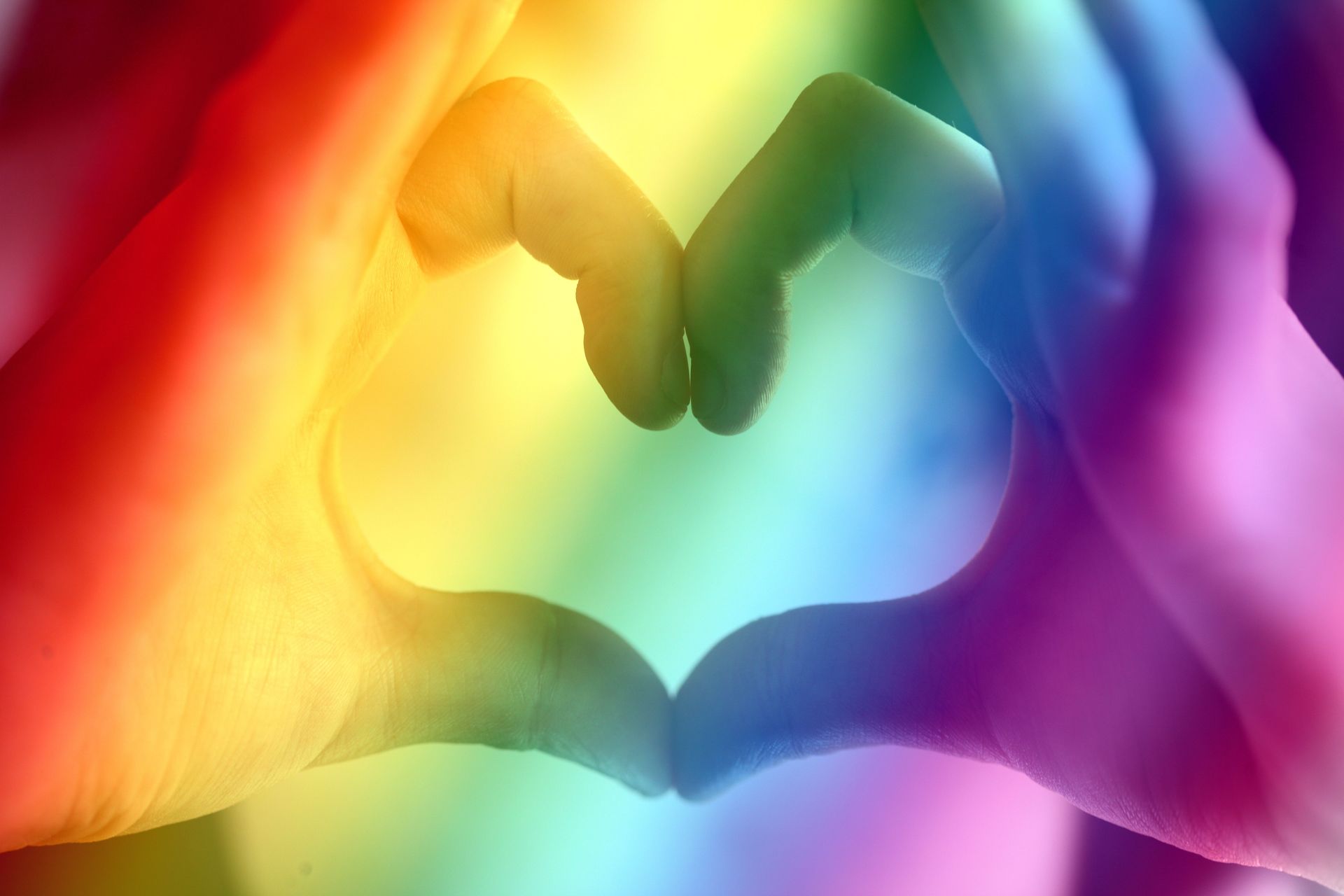 Hands forming a heart shape over a rainbow gradient background
