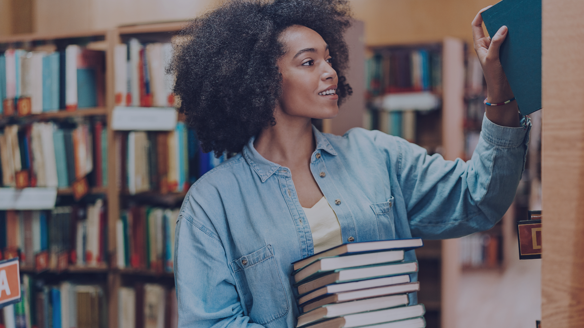 Person holding books and reaching for a shelf in a library