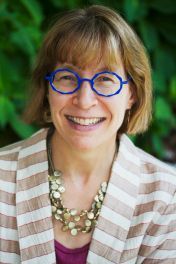 Smiling person with blue glasses and striped cardigan against a leafy green background