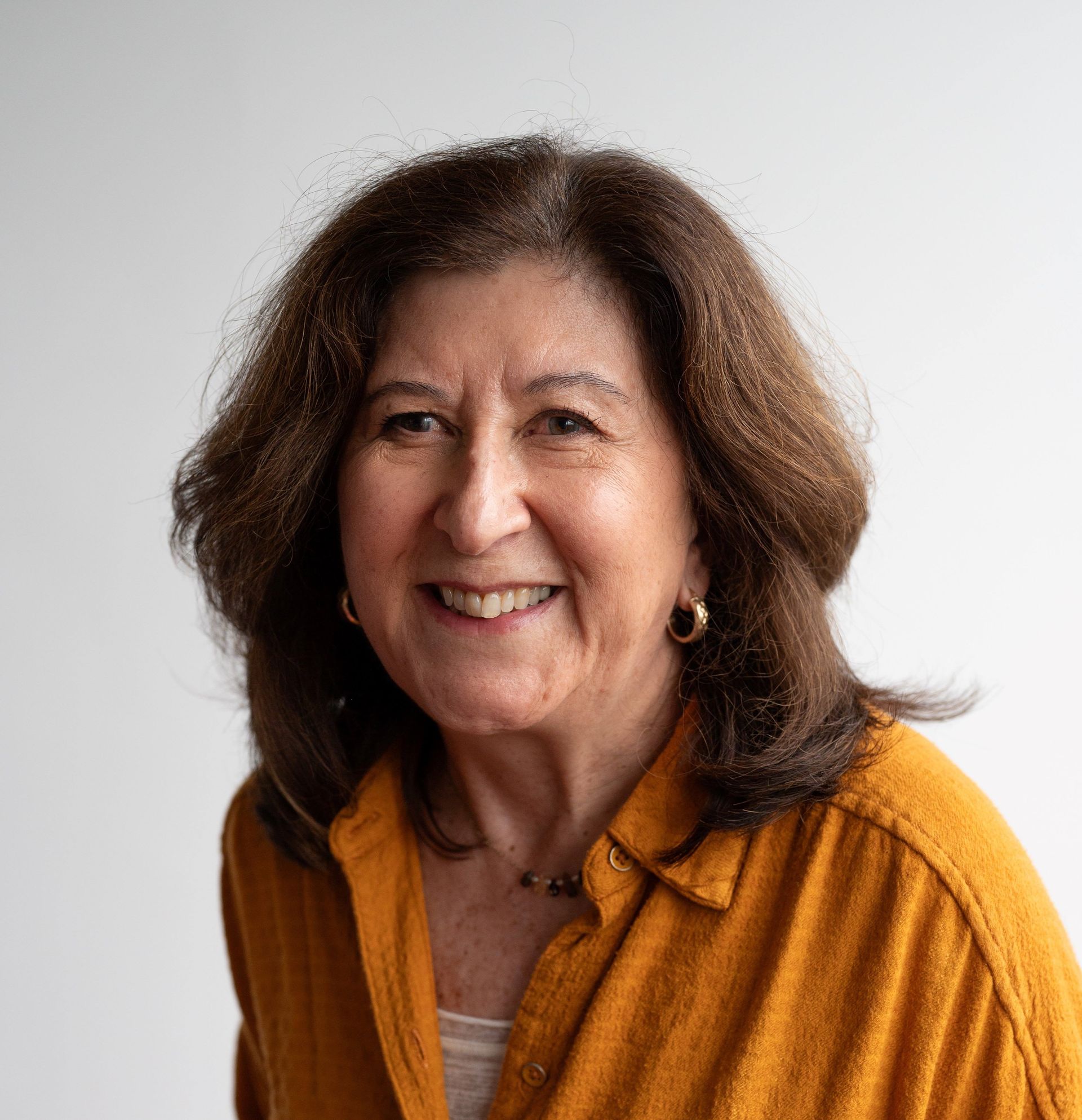 Smiling woman in a mustard yellow shirt against a light background