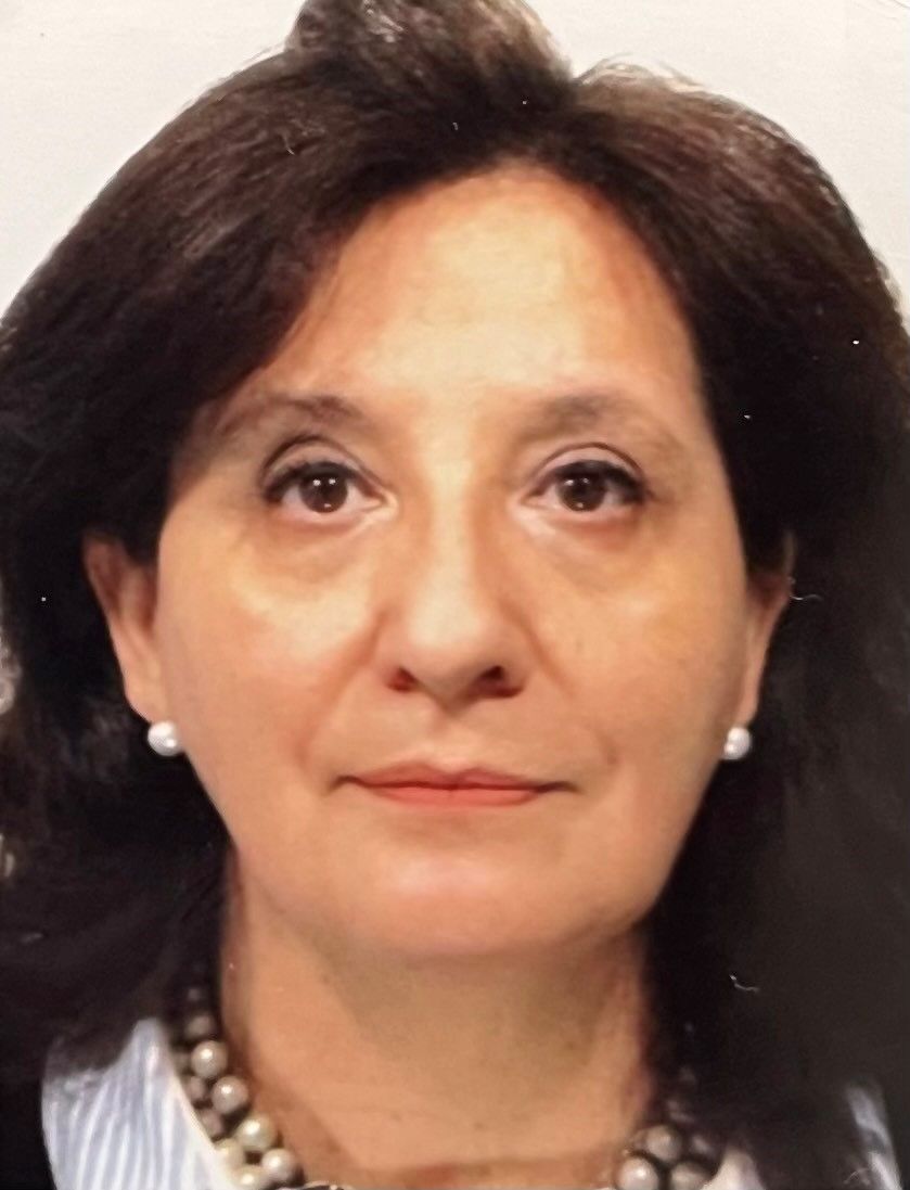 Portrait of a woman with dark hair, pearl earrings, and a necklace against a plain background