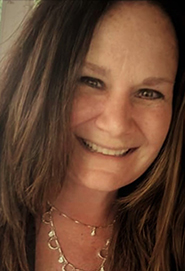 Smiling woman with long brown hair, wearing a necklace, in a close-up portrait.