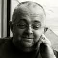 Smiling bald man with glasses resting his face on his hand by a window