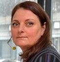 Close-up portrait of a woman with brown hair, looking at the camera indoors