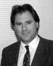 Black-and-white headshot of a man in a suit and tie, facing the camera.