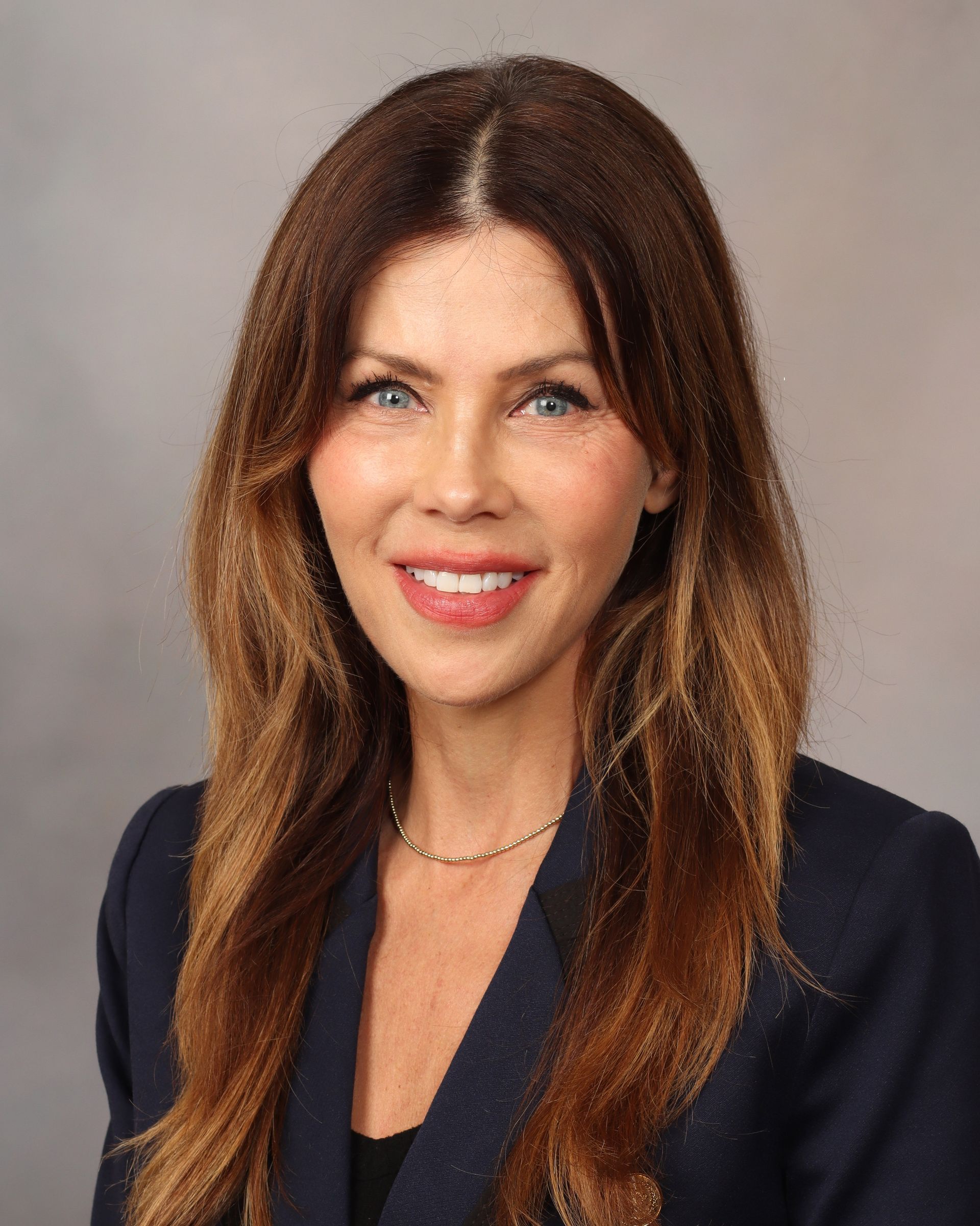 Portrait of a smiling woman with long brown hair in a navy blazer against a neutral background