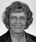 Black-and-white portrait of a smiling person with short curly hair and glasses