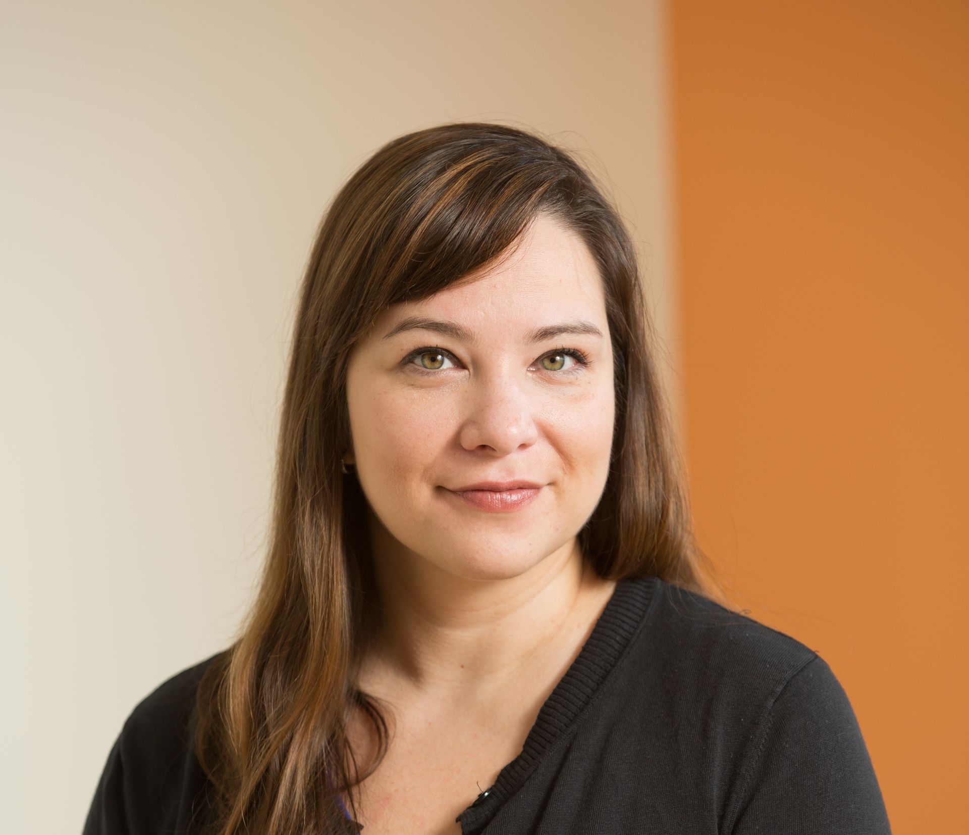 Portrait of a smiling woman with brown hair against a beige and orange background