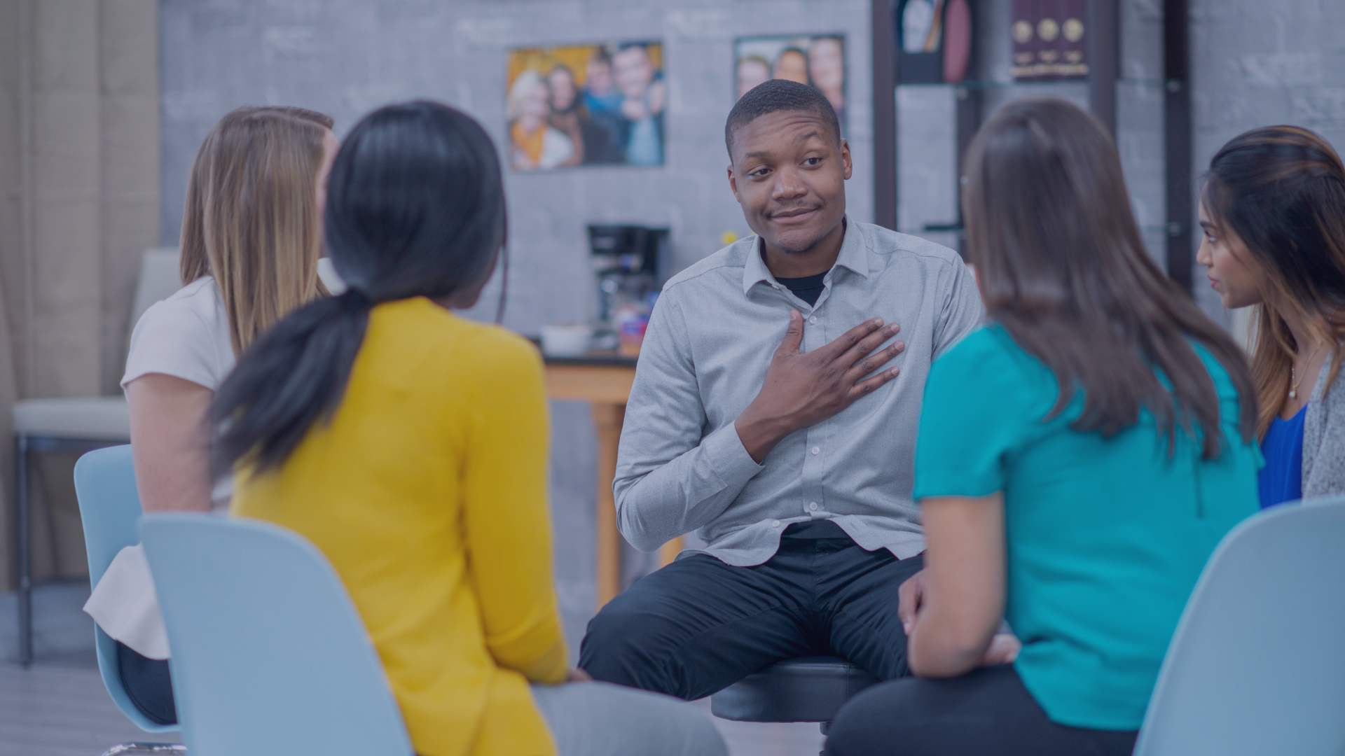 Small group in a bright room listens to a man speaking during a seated discussion.