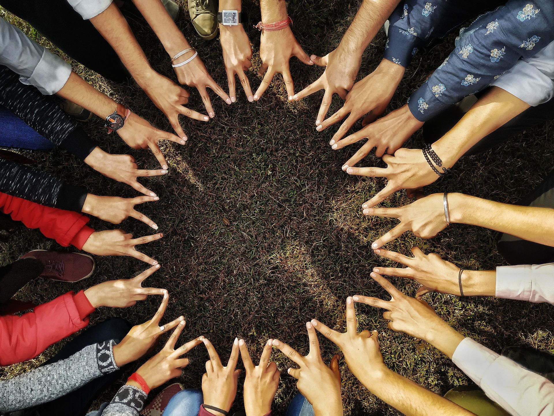 Many hands joined in a circle around a dark center on a textured ground.