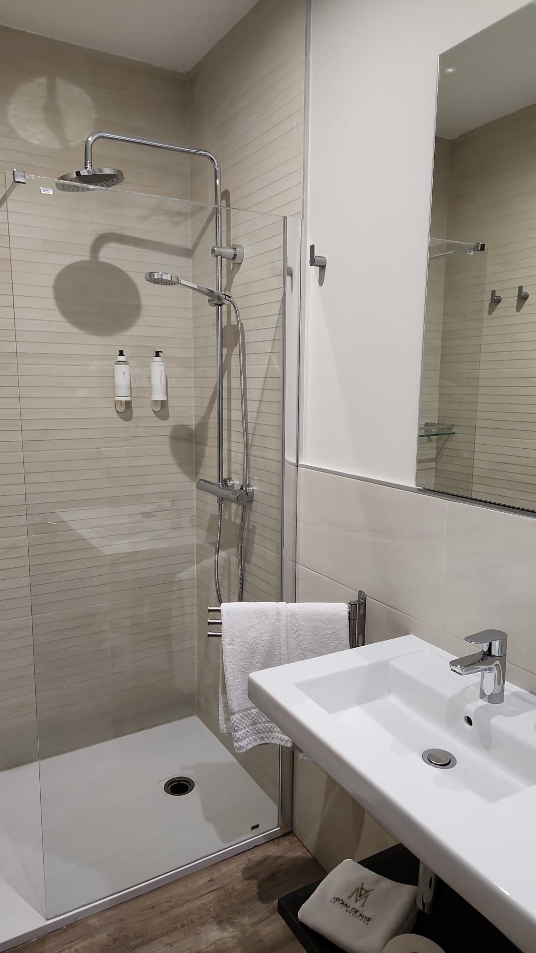 Baño de hotel moderno con ducha, lavabo y espejo; colores neutros.