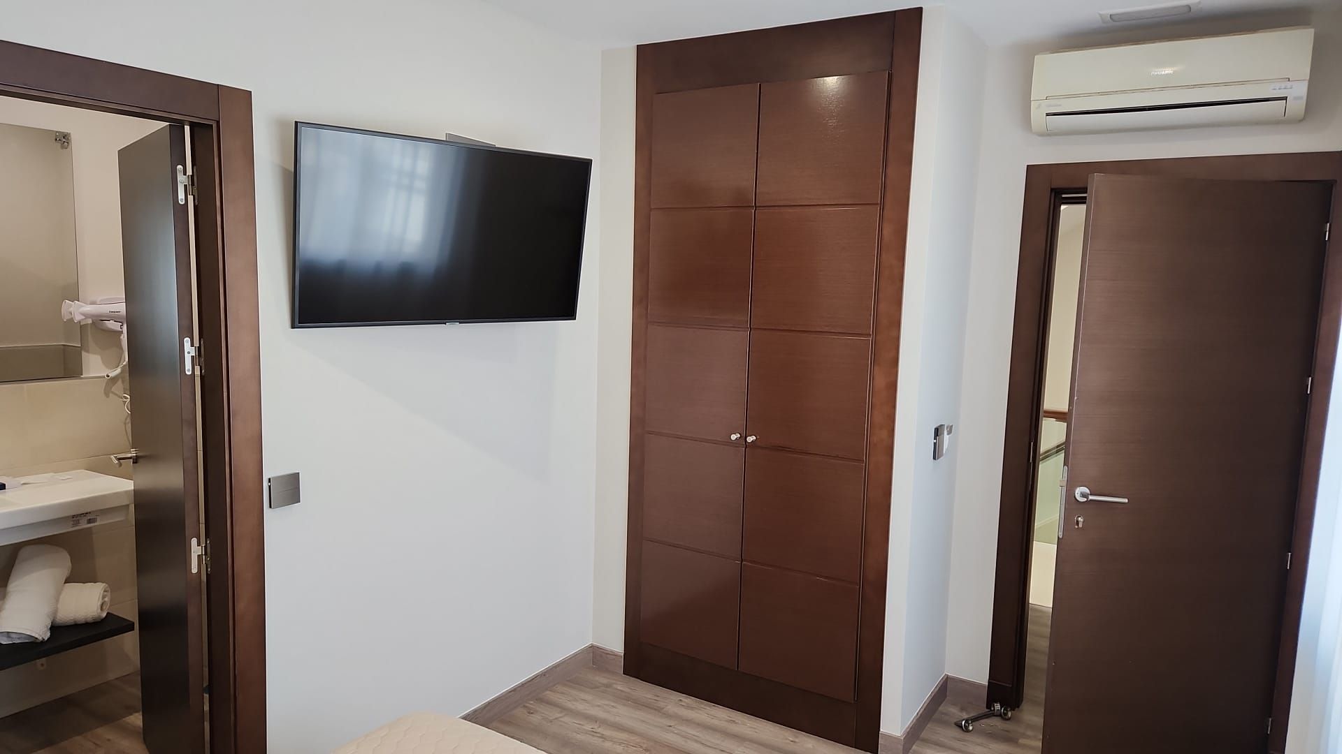 Un dormitorio con TV, armario y dos puertas que conducen a un baño y una segunda habitación.