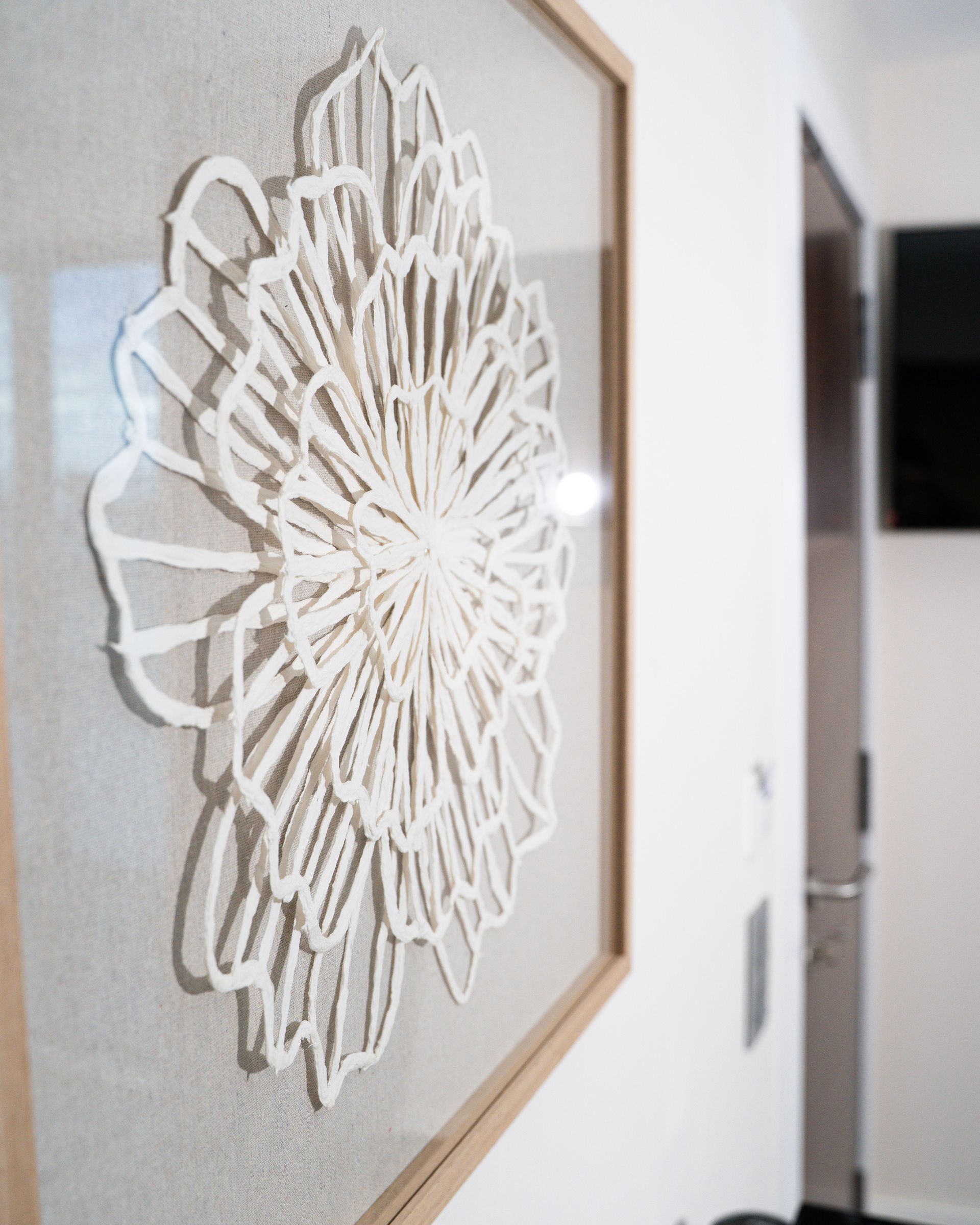 Arte floral en papel blanco en un marco de madera sobre una pared blanca.