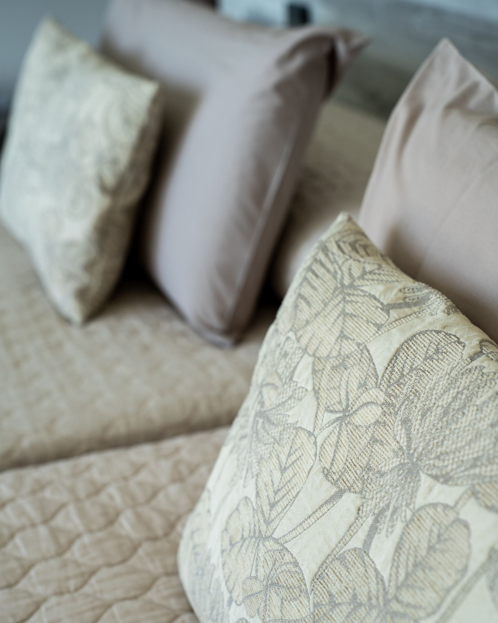 Primer plano de almohadas beige con diseño floral sobre una cama con funda acolchada.