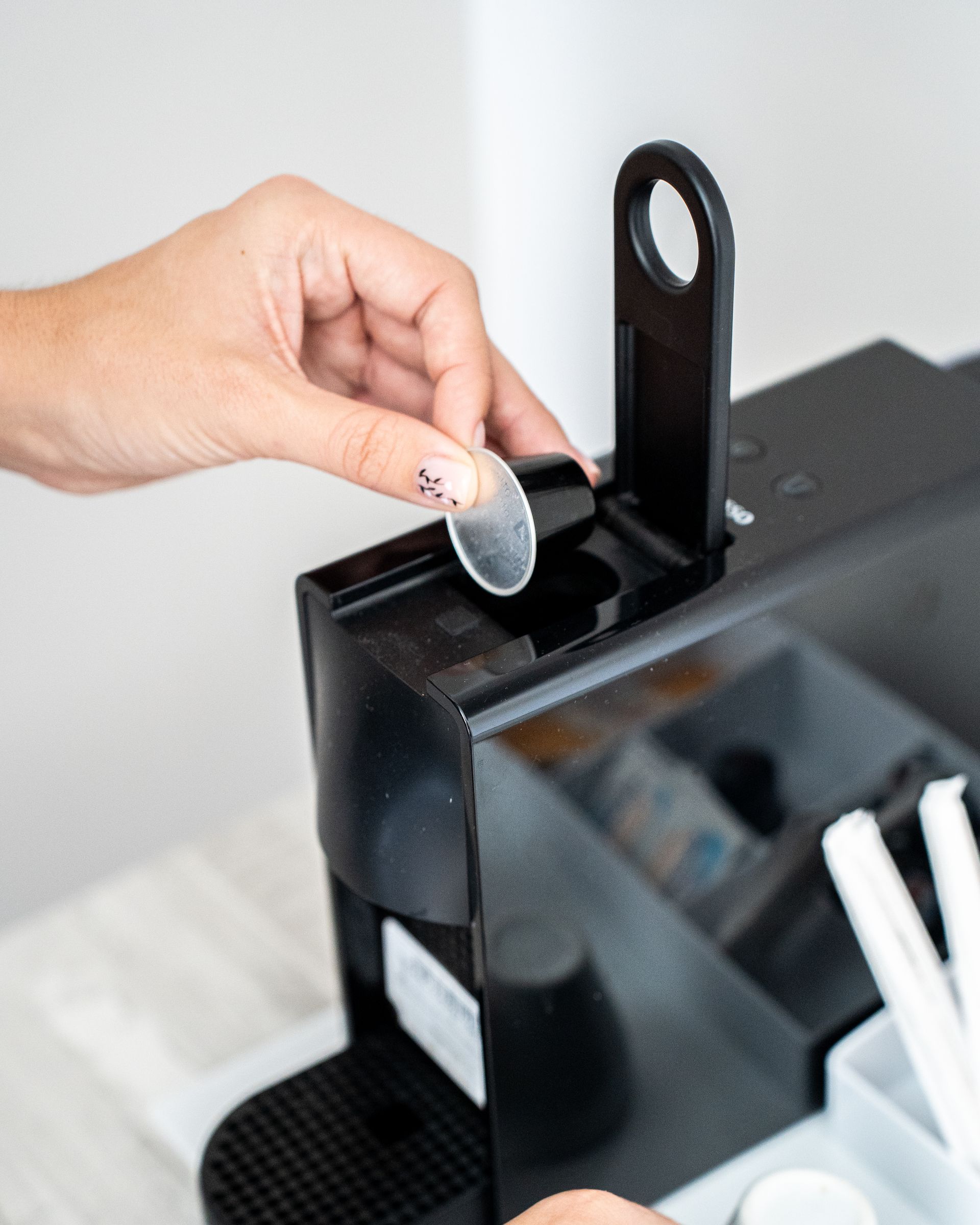 Una persona inserta un pequeño disco de plástico transparente en una máquina de café negro.