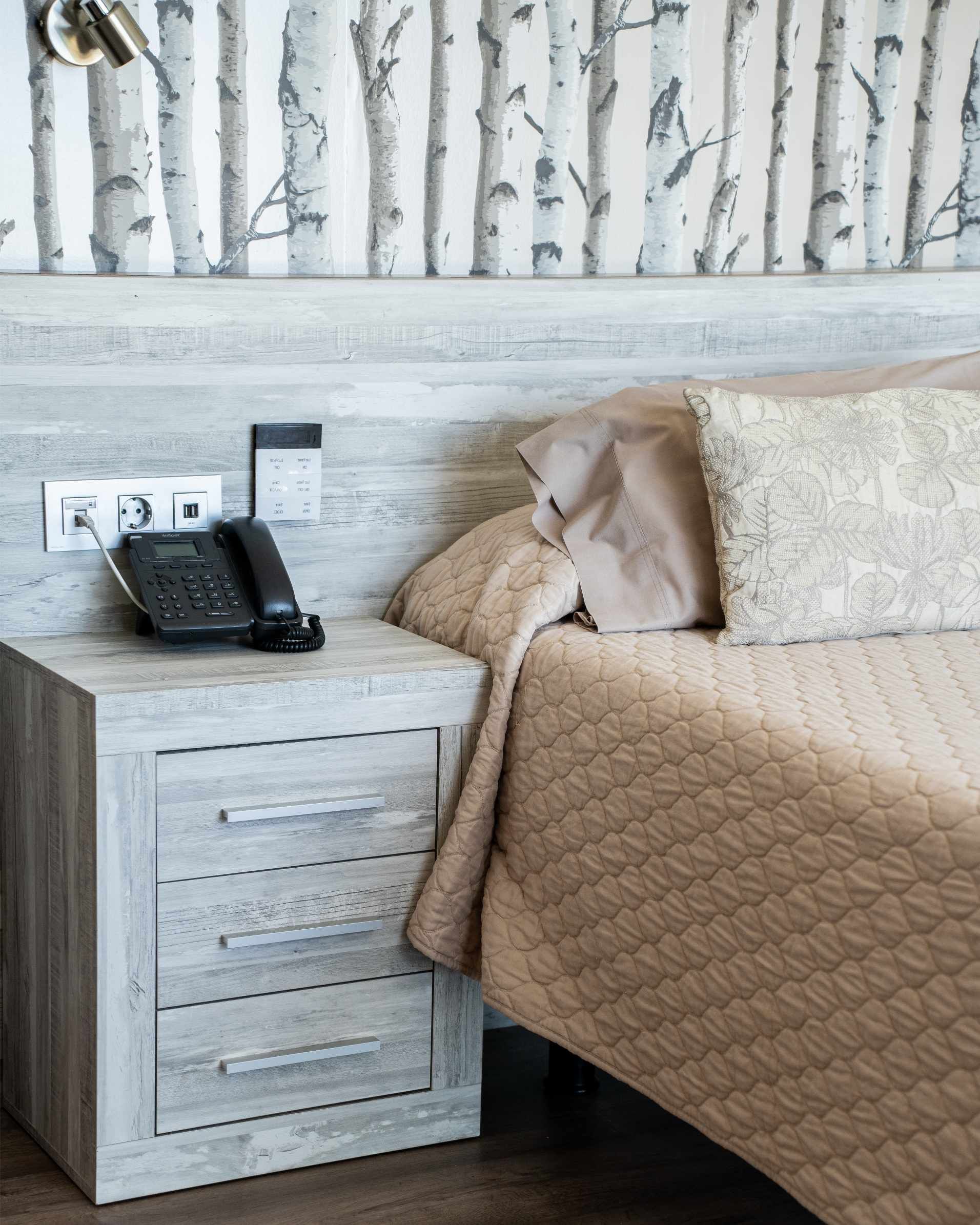 Dormitorio con mesita de noche, cama, papel pintado con estampado de abedul y teléfono.