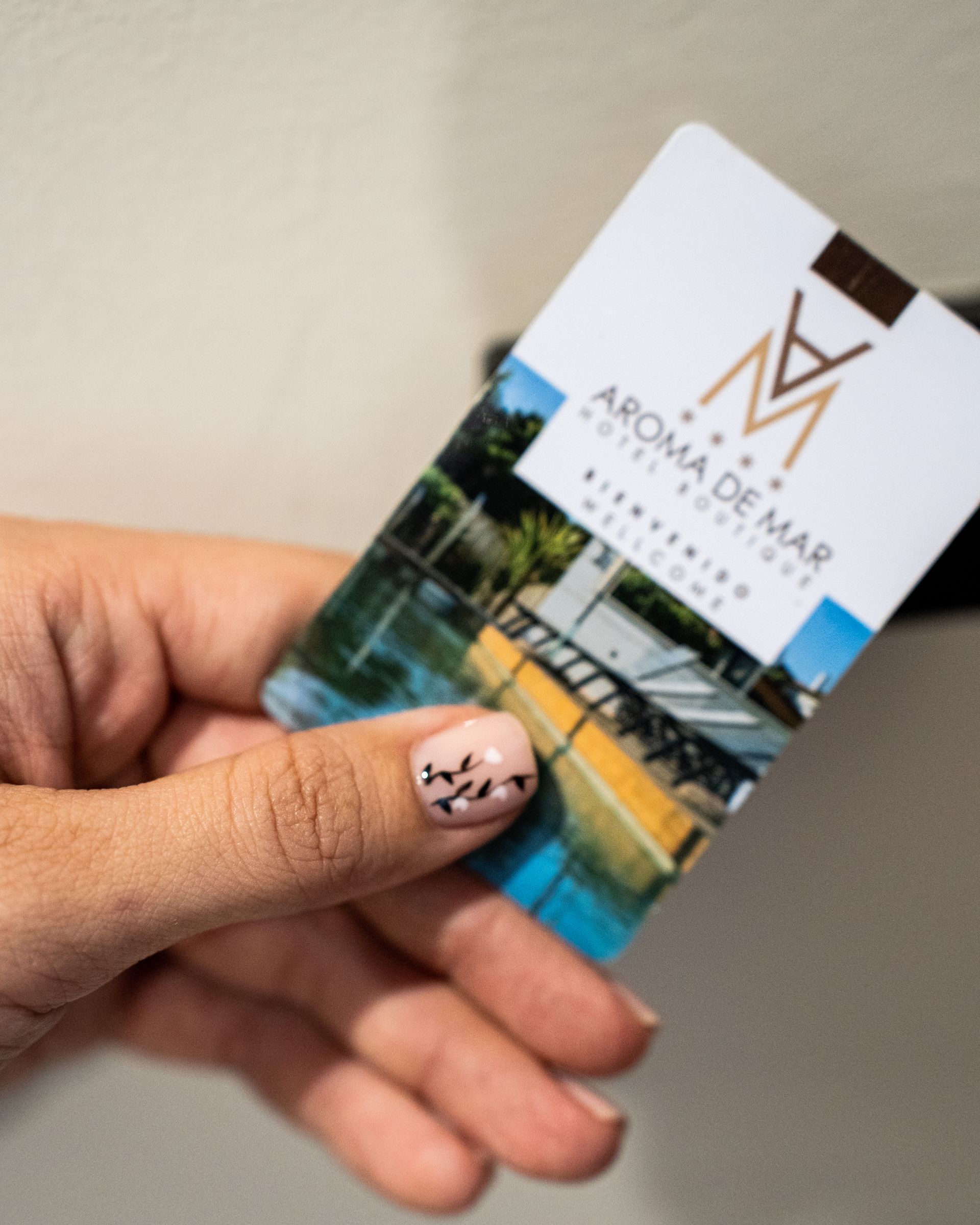 Mano sosteniendo una tarjeta de acceso del Hotel Aroma de Mar, con una foto de un paisaje y el logotipo del hotel.