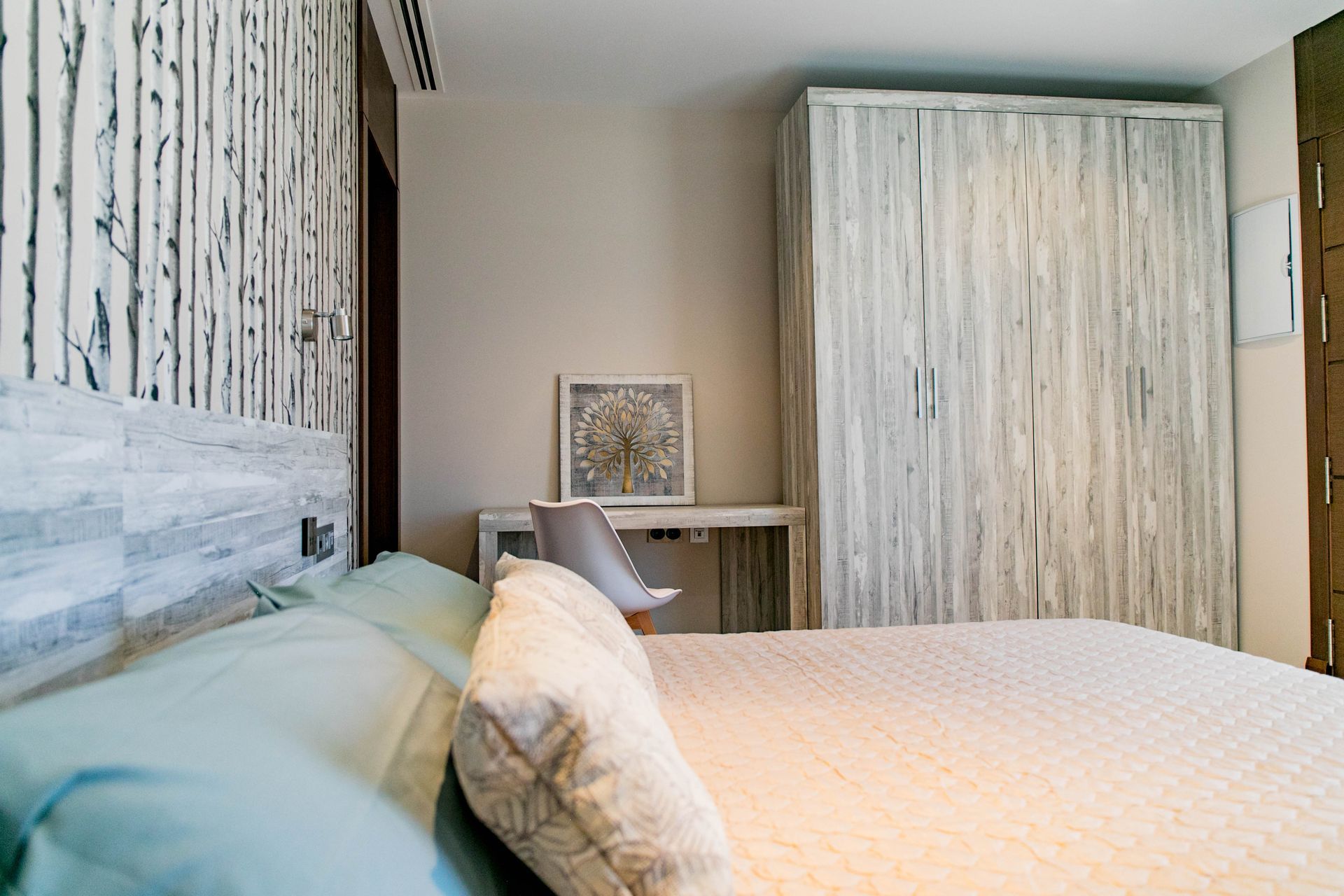 Dormitorio con ropa de cama azul claro, escritorio y silla blancos, armario blanco texturizado.