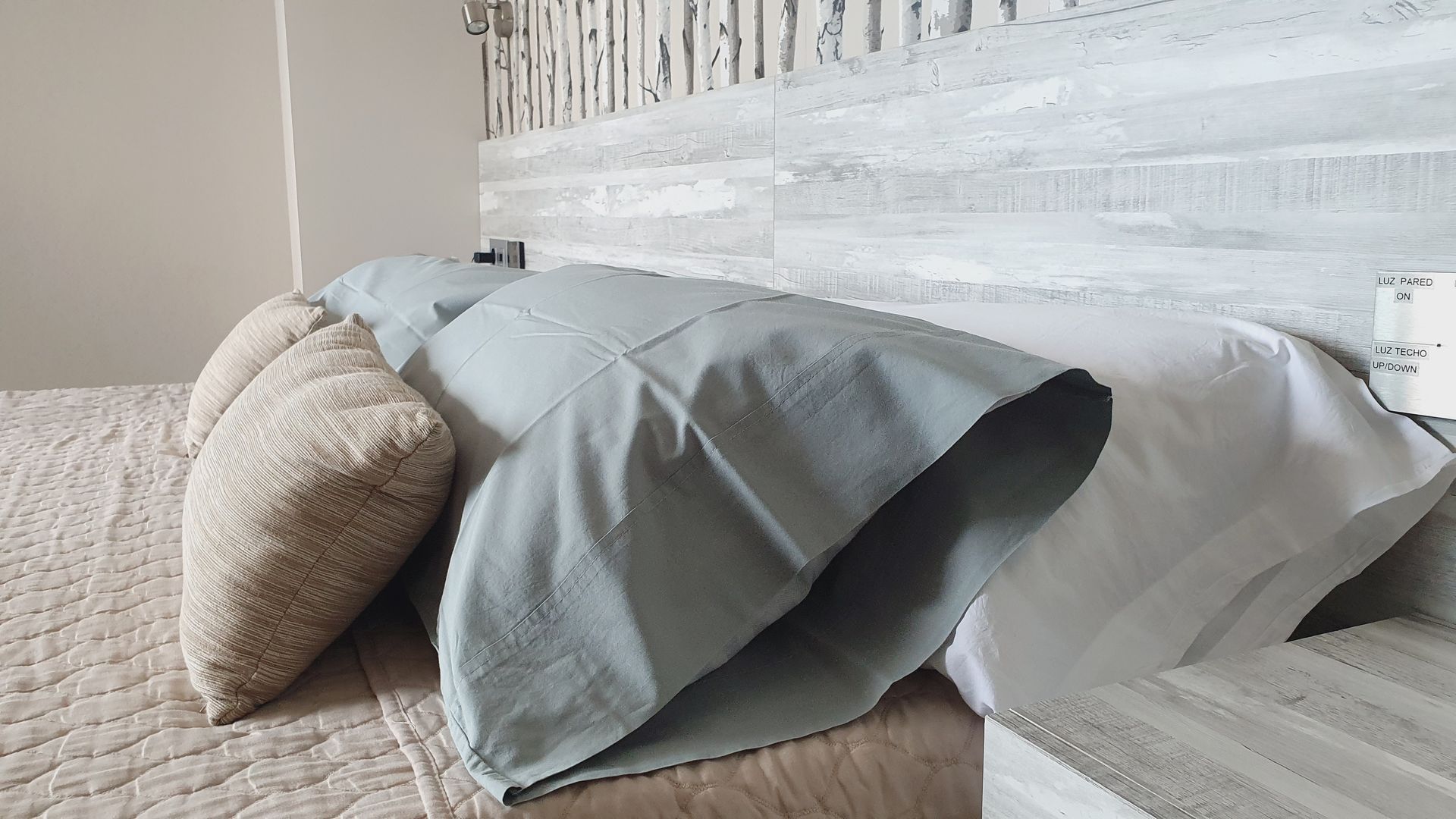Cama con almohadas en tonos azul, blanco y beige sobre un cabecero texturizado.