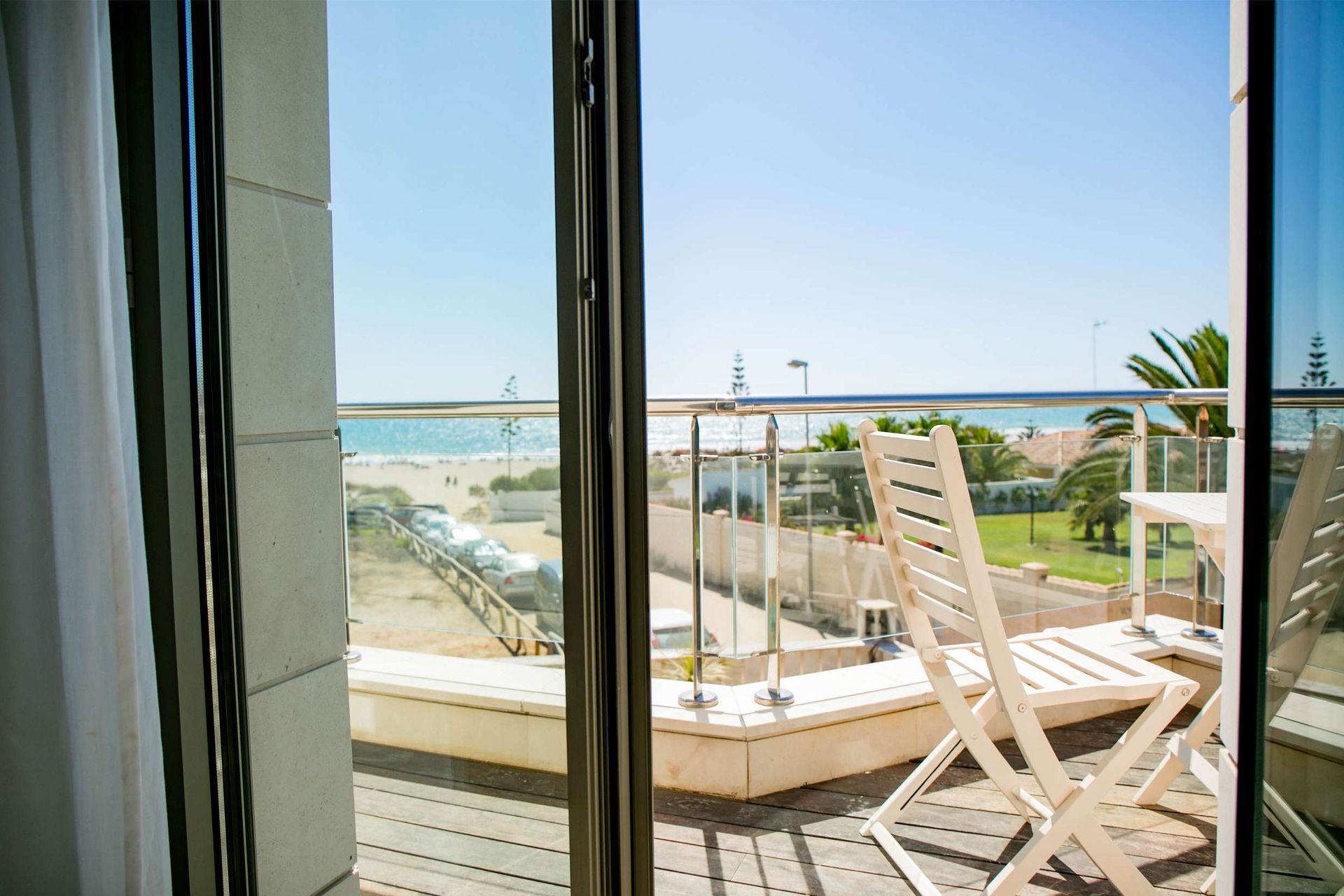Balcón con vista a la playa, sillas blancas, cielo azul, día soleado.