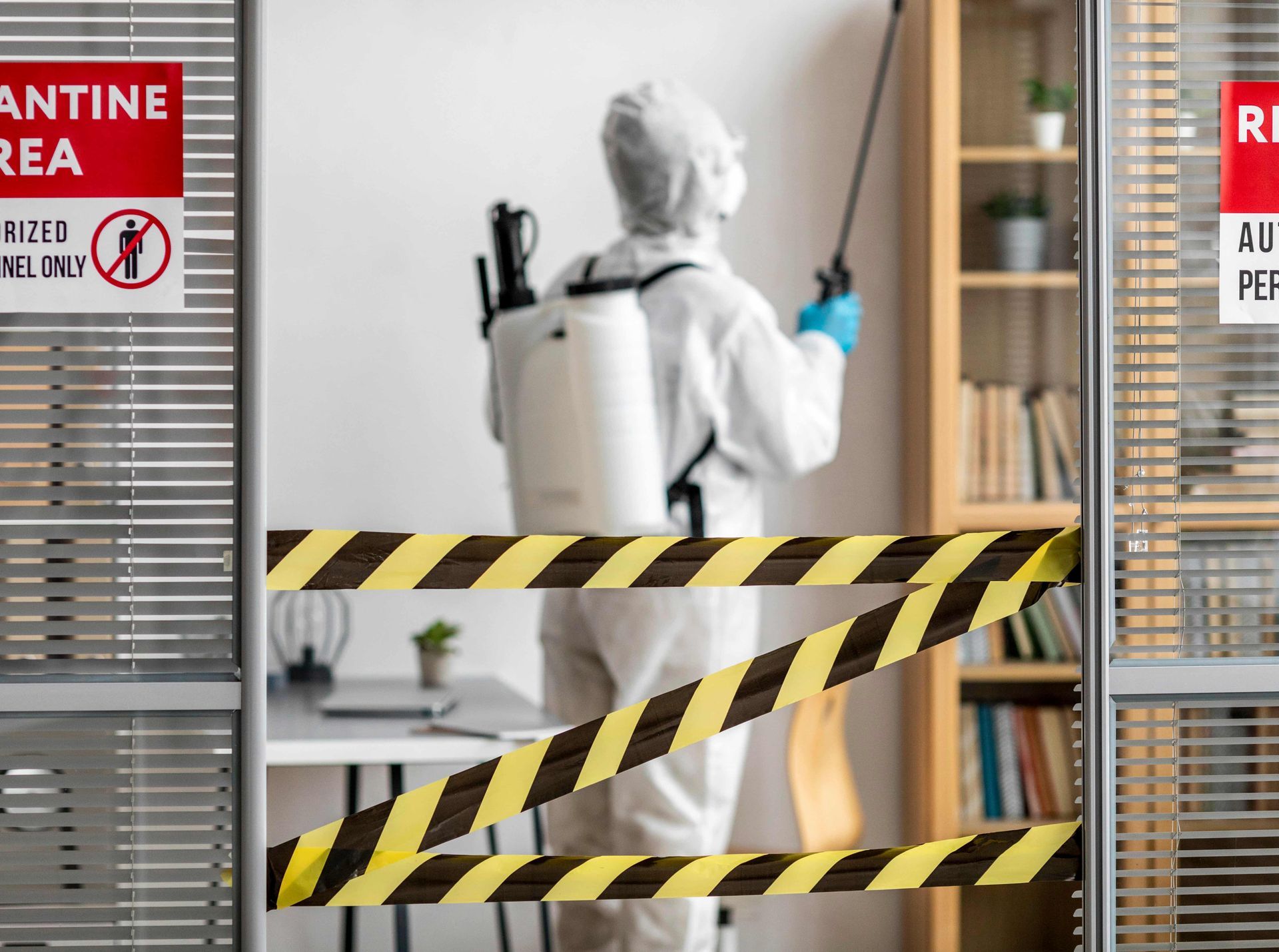 Person in hazmat suit spraying disinfectant in a quarantined office.