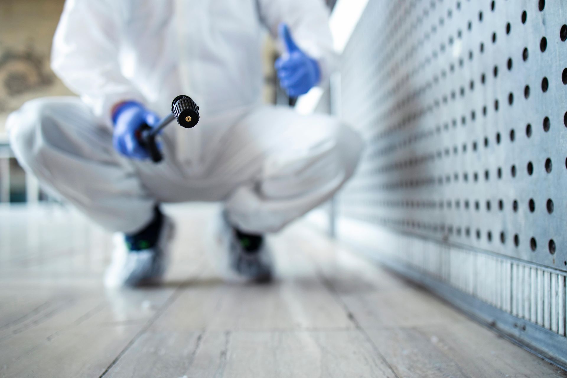 Person in white protective suit spraying a surface, giving thumbs up.