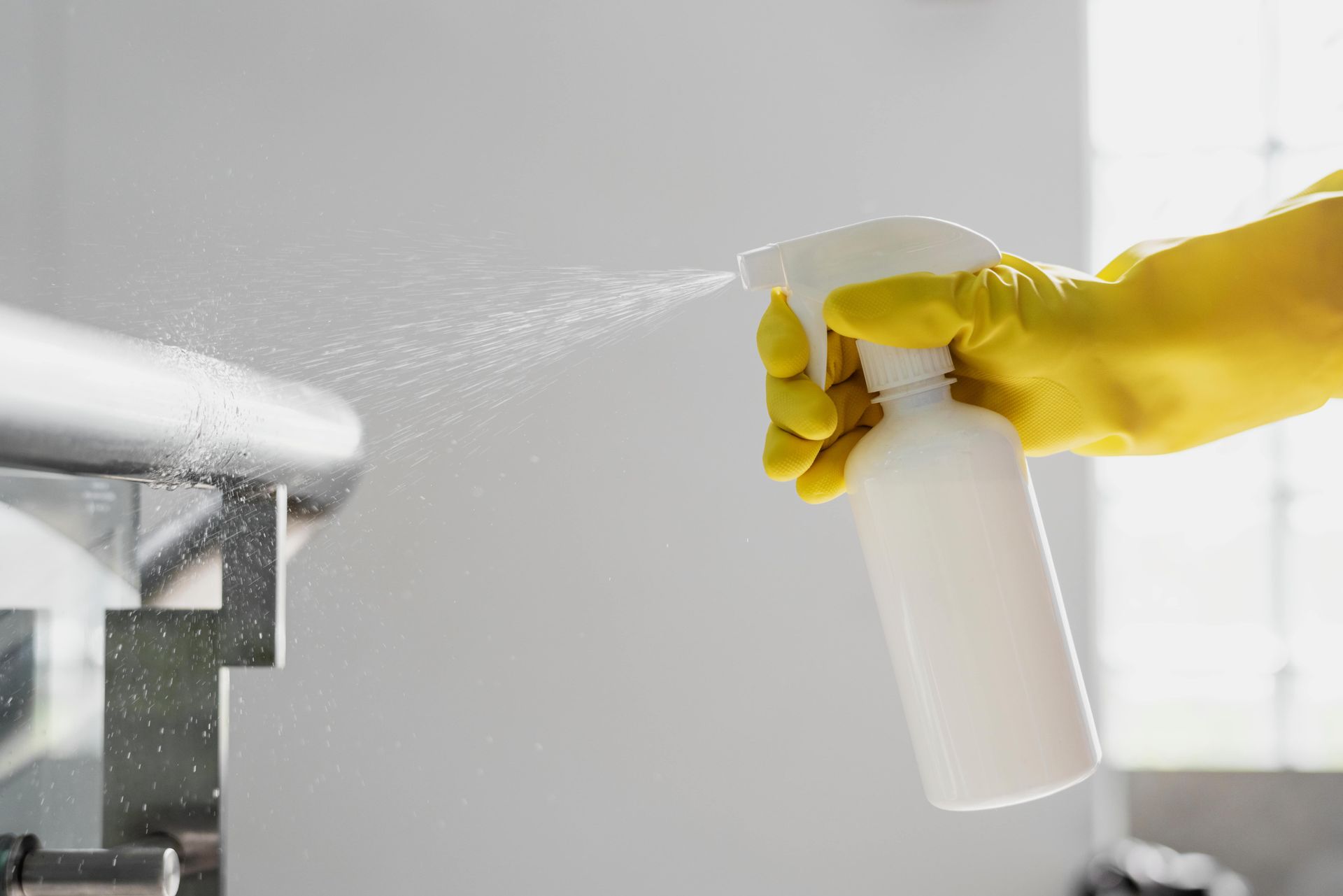 Hand in yellow glove sprays sanitizer onto a metal railing.