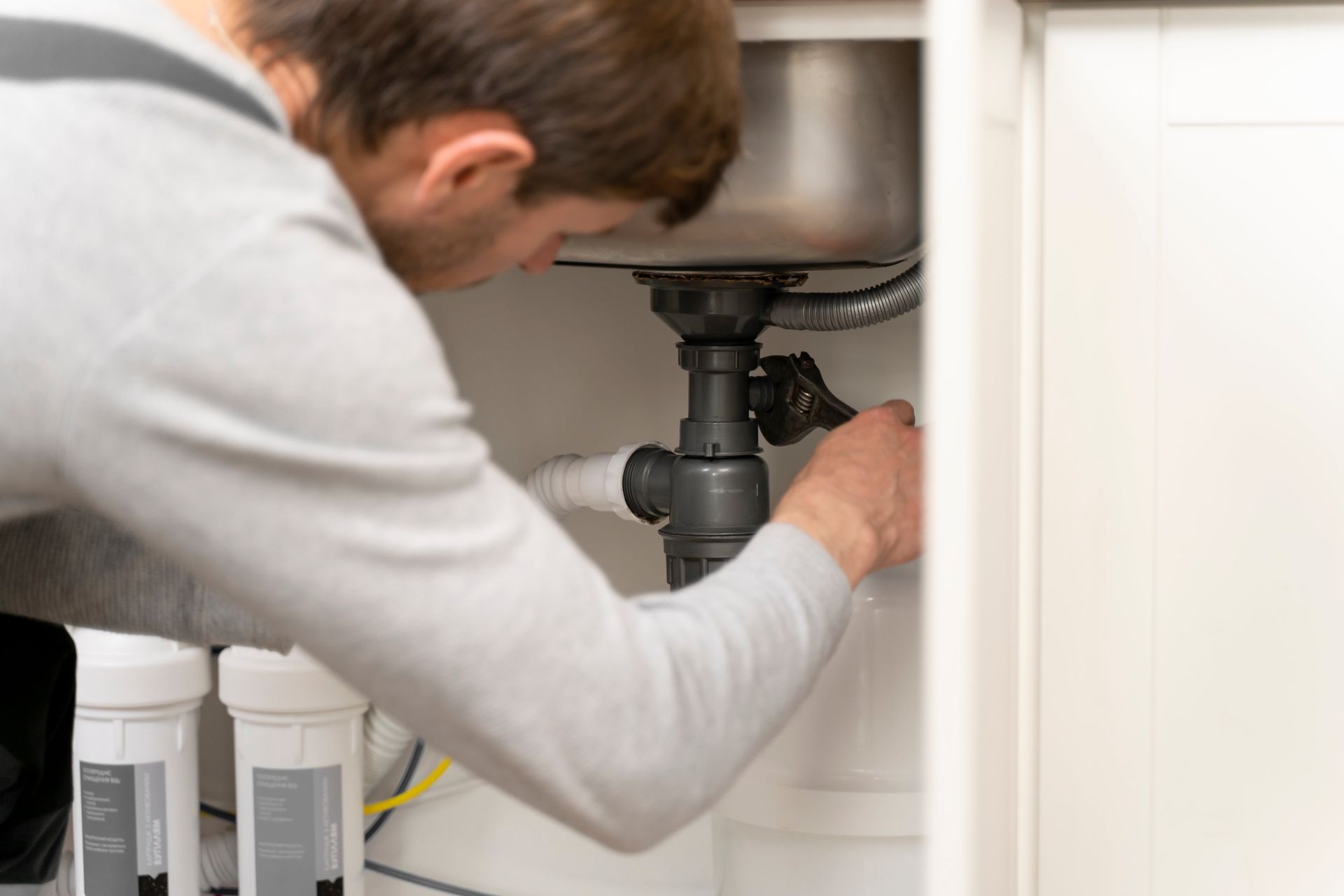 Person working on plumbing under a sink with a wrench.