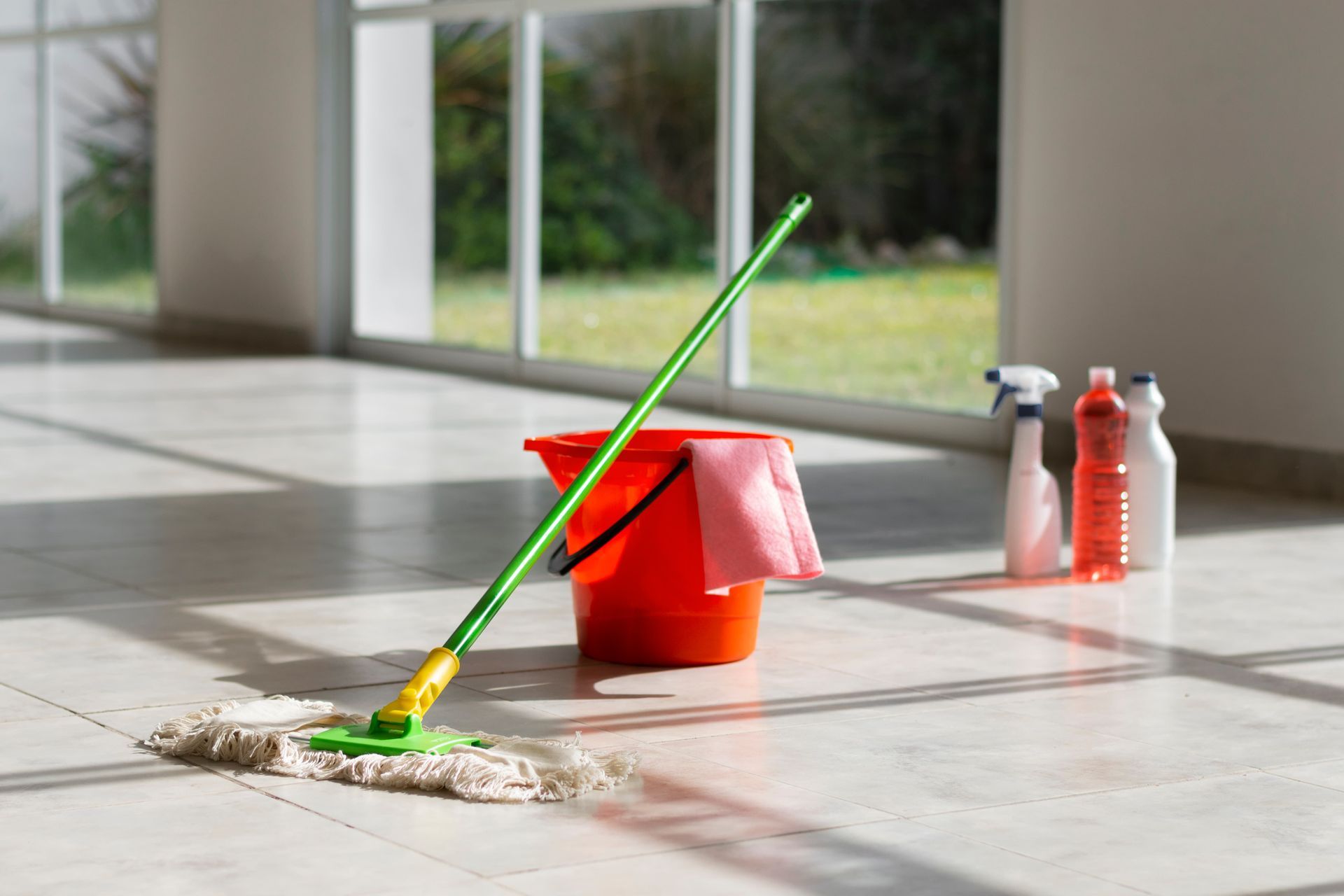 Mop, bucket, cleaning supplies on marble floor in sunlit room.