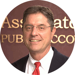 Man in glasses, smiling, wearing a suit and red tie; background says