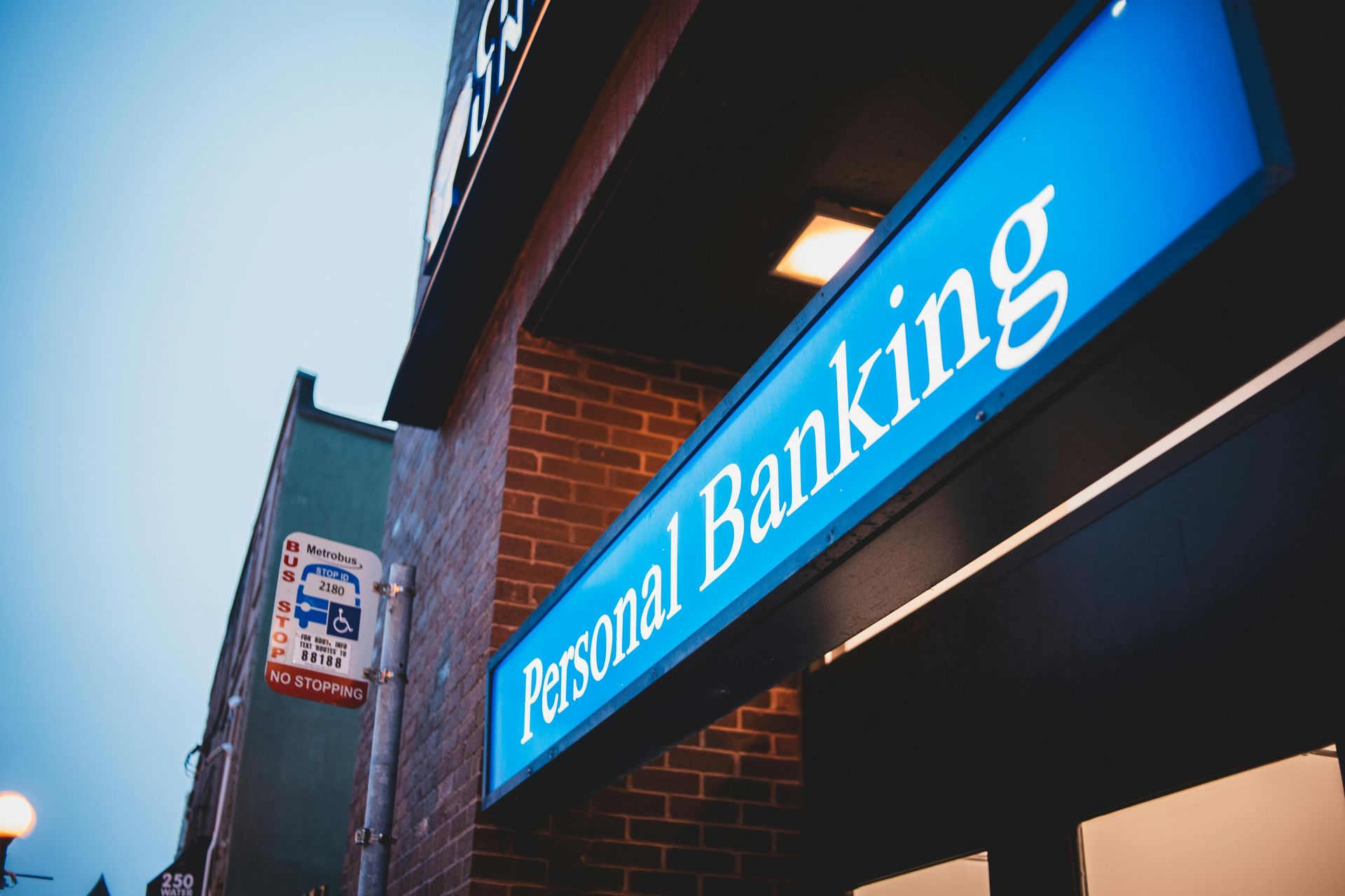 Blue sign reading “Personal Banking” on a brick building exterior at dusk