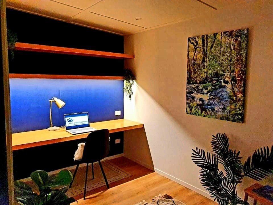 A living room with a desk with a laptop on it and a painting on the wall.