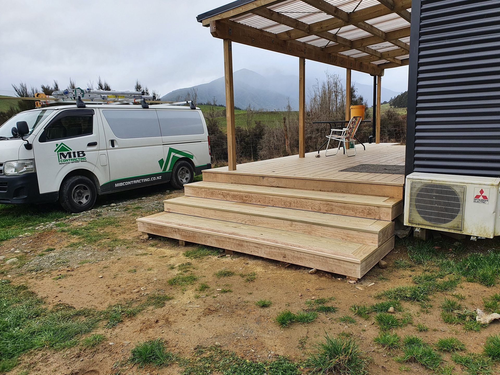 A white van is parked in front of a house with wooden steps.
