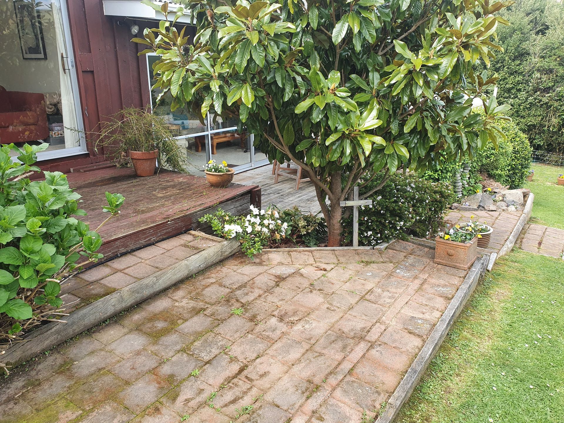 A brick walkway leading to a house with a tree and a cross.