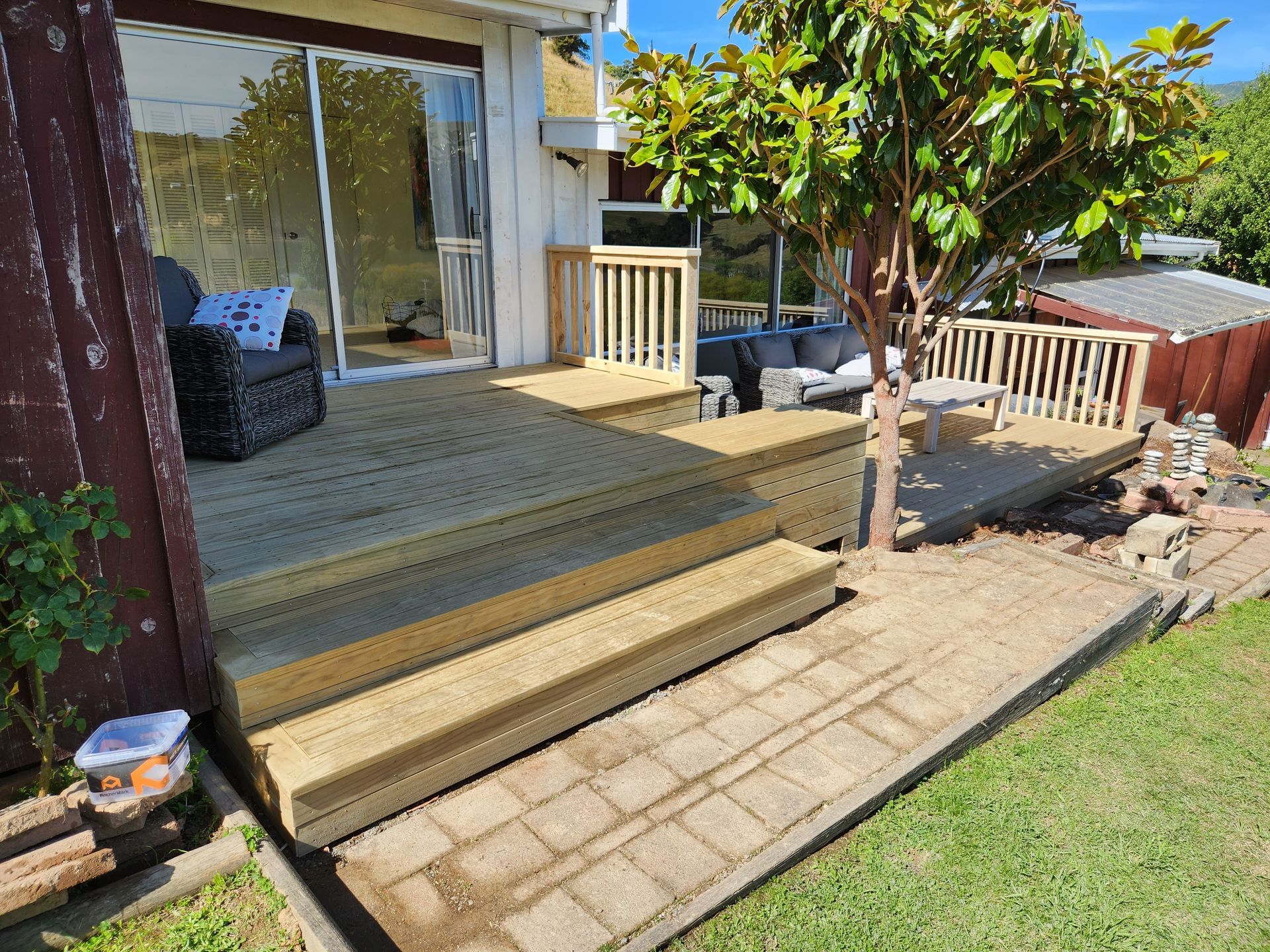 A wooden deck with stairs leading up to it is in the backyard of a house.