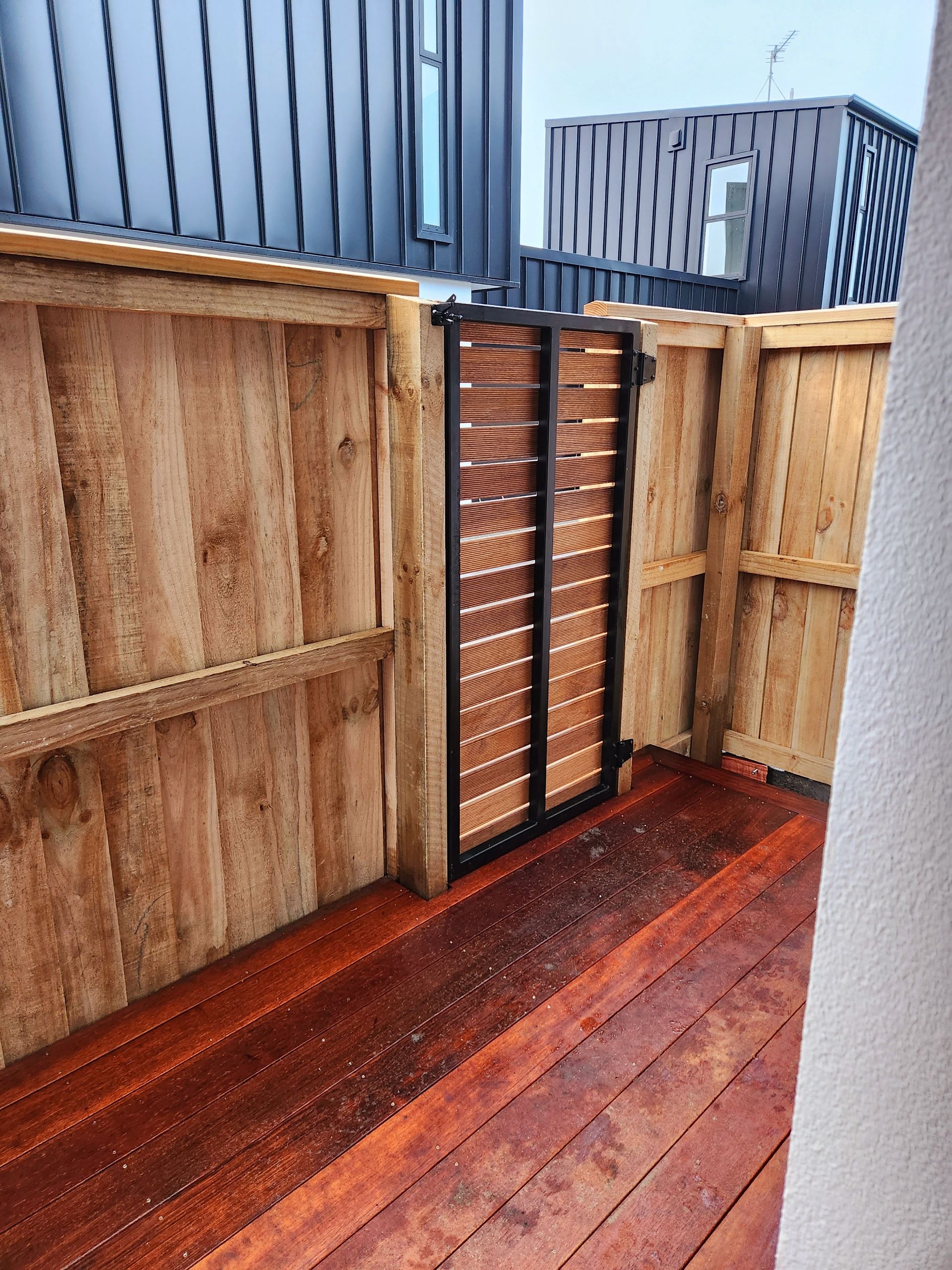 A wooden deck with a wooden fence and a metal gate.